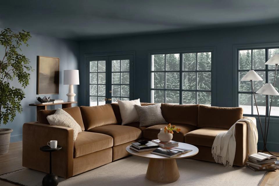 Modern living room with caramel leather sectional, teal walls, and abundant natural light from gridded windows