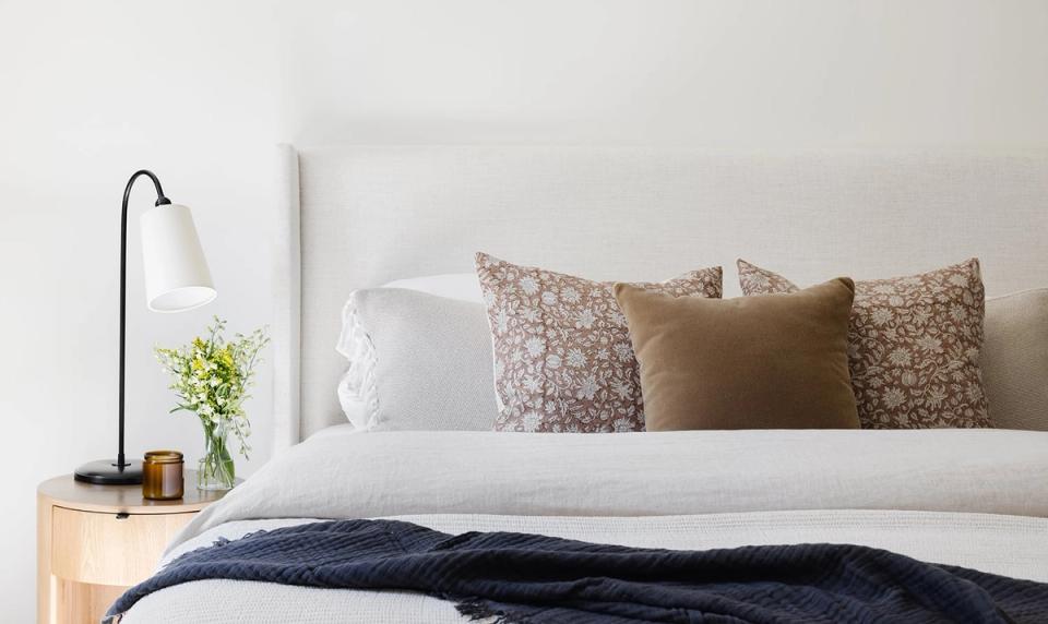 Contemporary bed detail with white linens, patterned throw pillows in earth tones, and warm wood nightstand against crisp white headboard