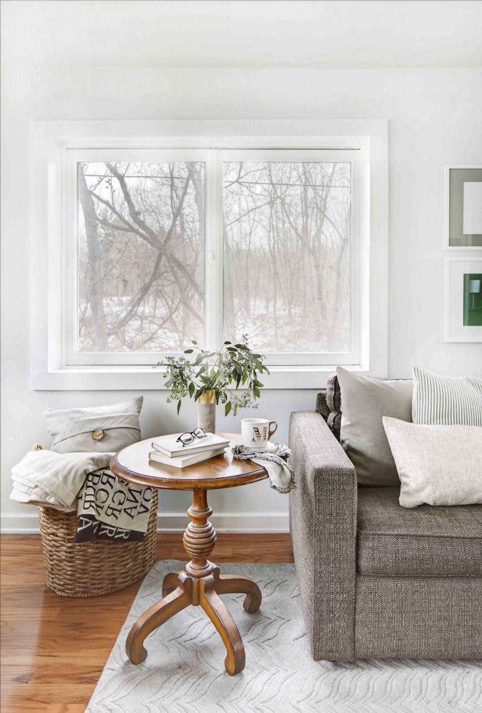 Scandinavian-inspired cozy nook with gray sofa, wooden pedestal table, and winter forest view