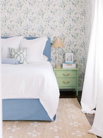 Cottage-style bedroom with soft floral wallpapered accent wall, blue bed base, and green nightstand