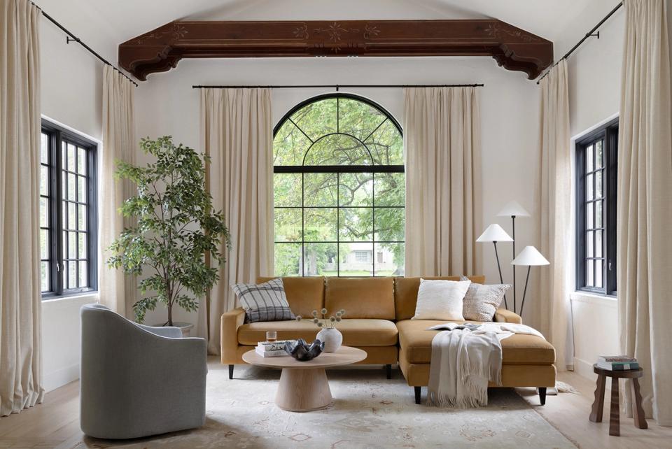 Transitional living room blending caramel sofa with soft neutrals, arched windows, dark wood beam