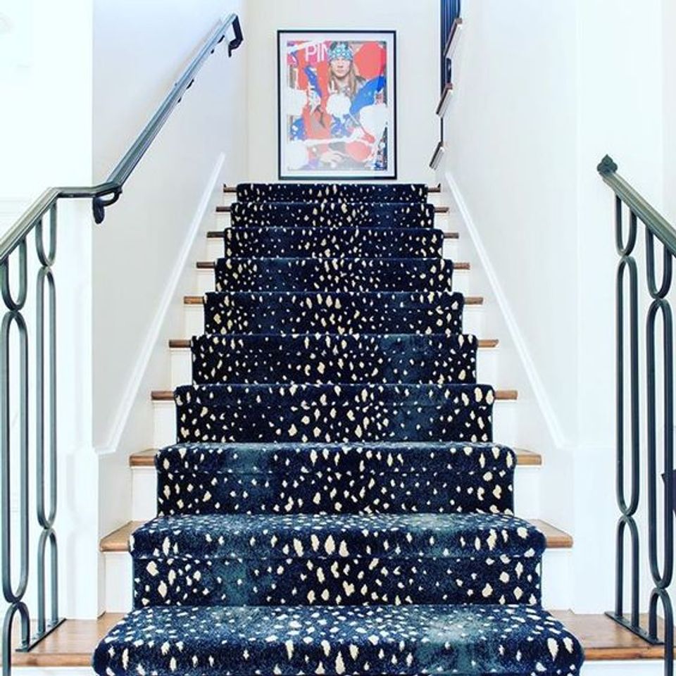 Modern staircase with navy and white speckled runner, mint-green railings, and colorful abstract art at landing