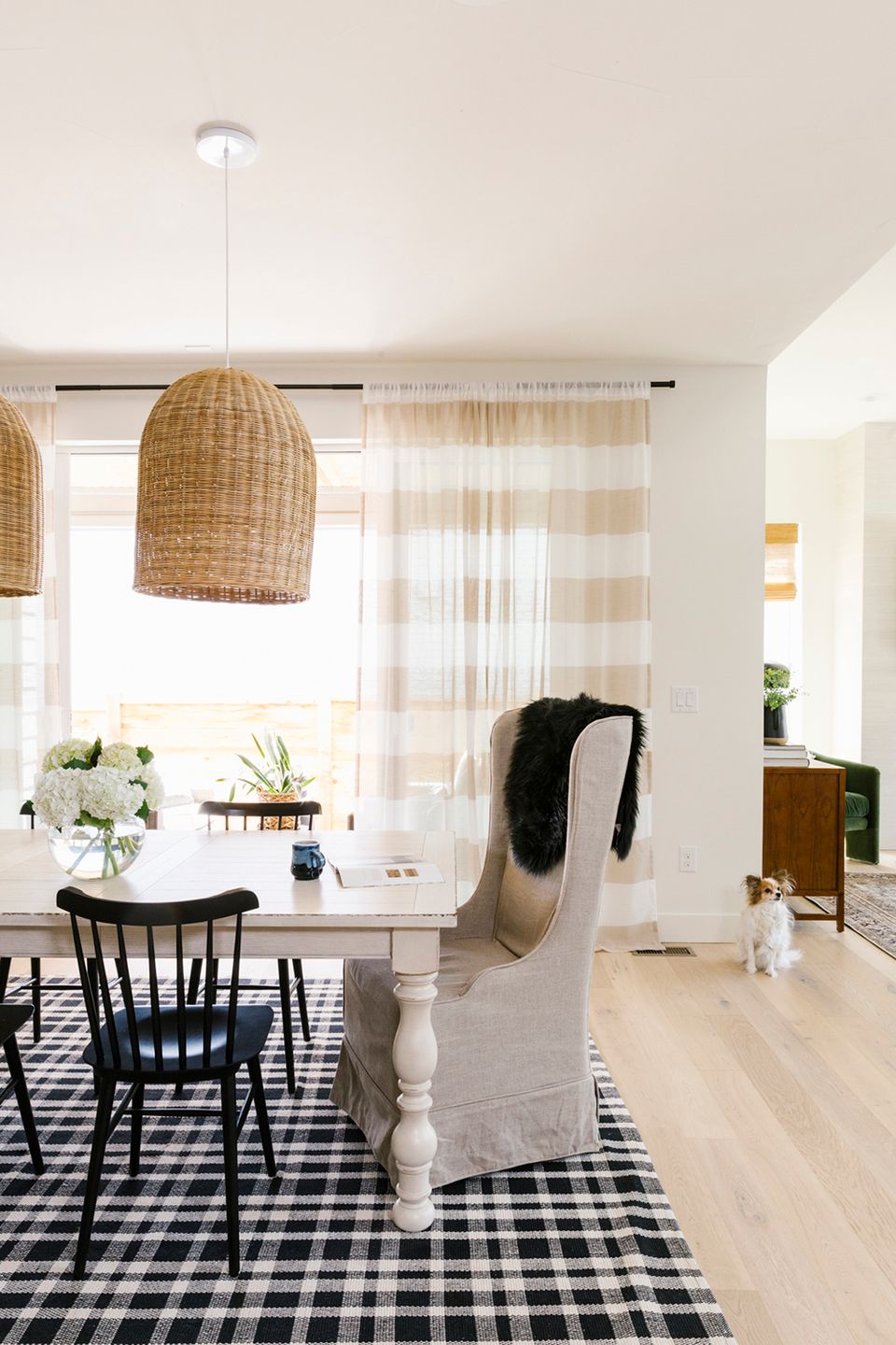 Bright farmhouse dining space with natural woven pendant lights, crisp black and white gingham rug, and soft neutral palette with shiplap accents