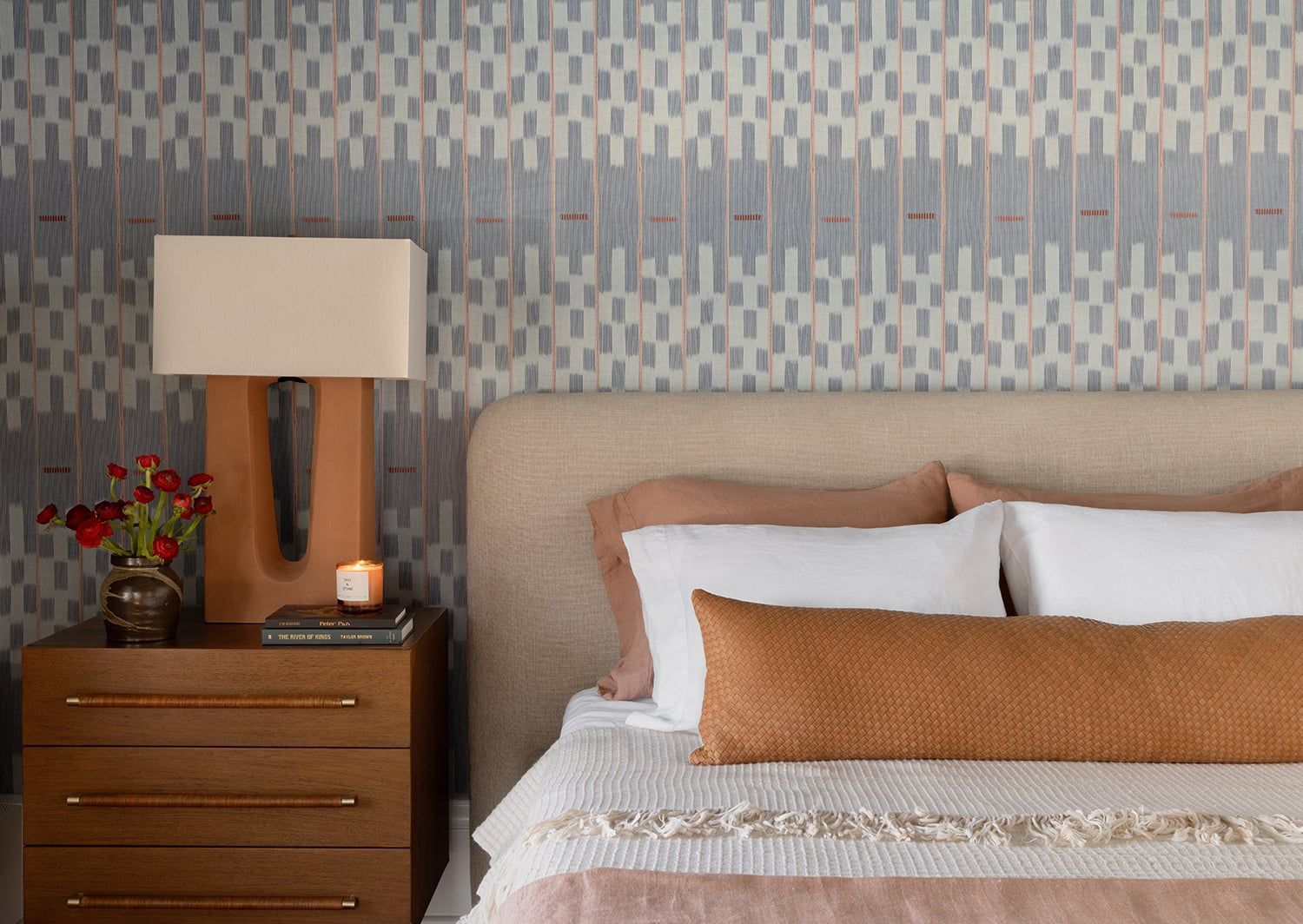 Modern bedroom with warm cognac and cream pillow arrangement against geometric patterned headboard wall
