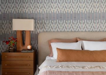 Modern bedroom with warm cognac and cream pillow arrangement against geometric patterned headboard wall