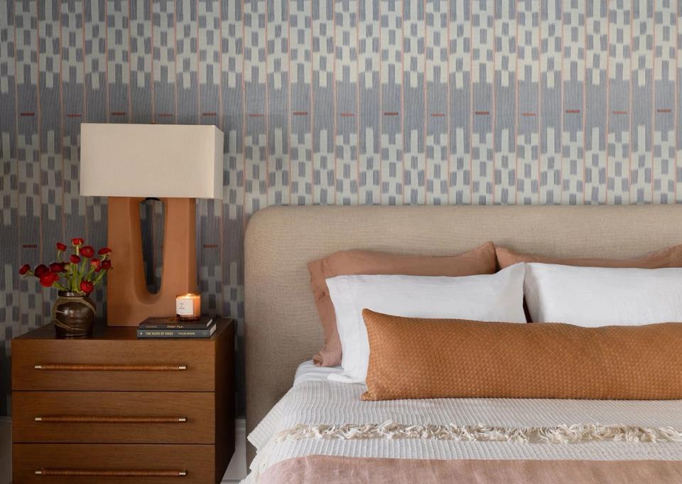 Modern bedroom with warm cognac and cream pillow arrangement against geometric patterned headboard wall