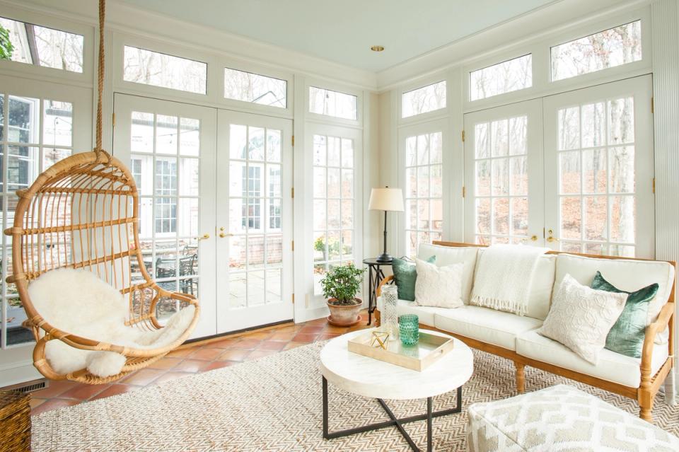Bright coastal sunroom with natural rattan hanging chair and woven seating, cream and green palette