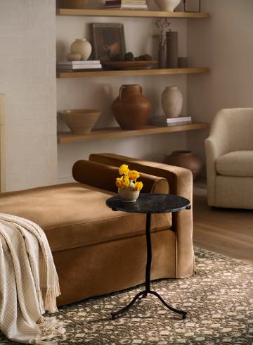 Warm, layered living space combining vintage leather, warm wood shelving, natural pottery, and soft neutral tones