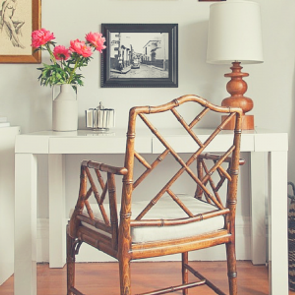 Eclectic workspace blending vintage rattan chair with white desk, coral florals, and warm wood tones