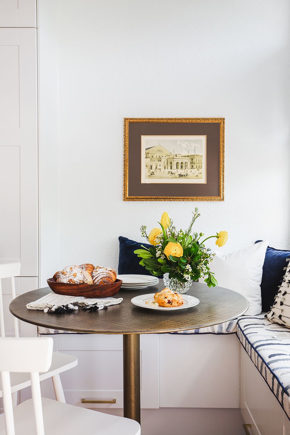 Transitional nook with round pedestal table, yellow flowers, and classic framed artwork