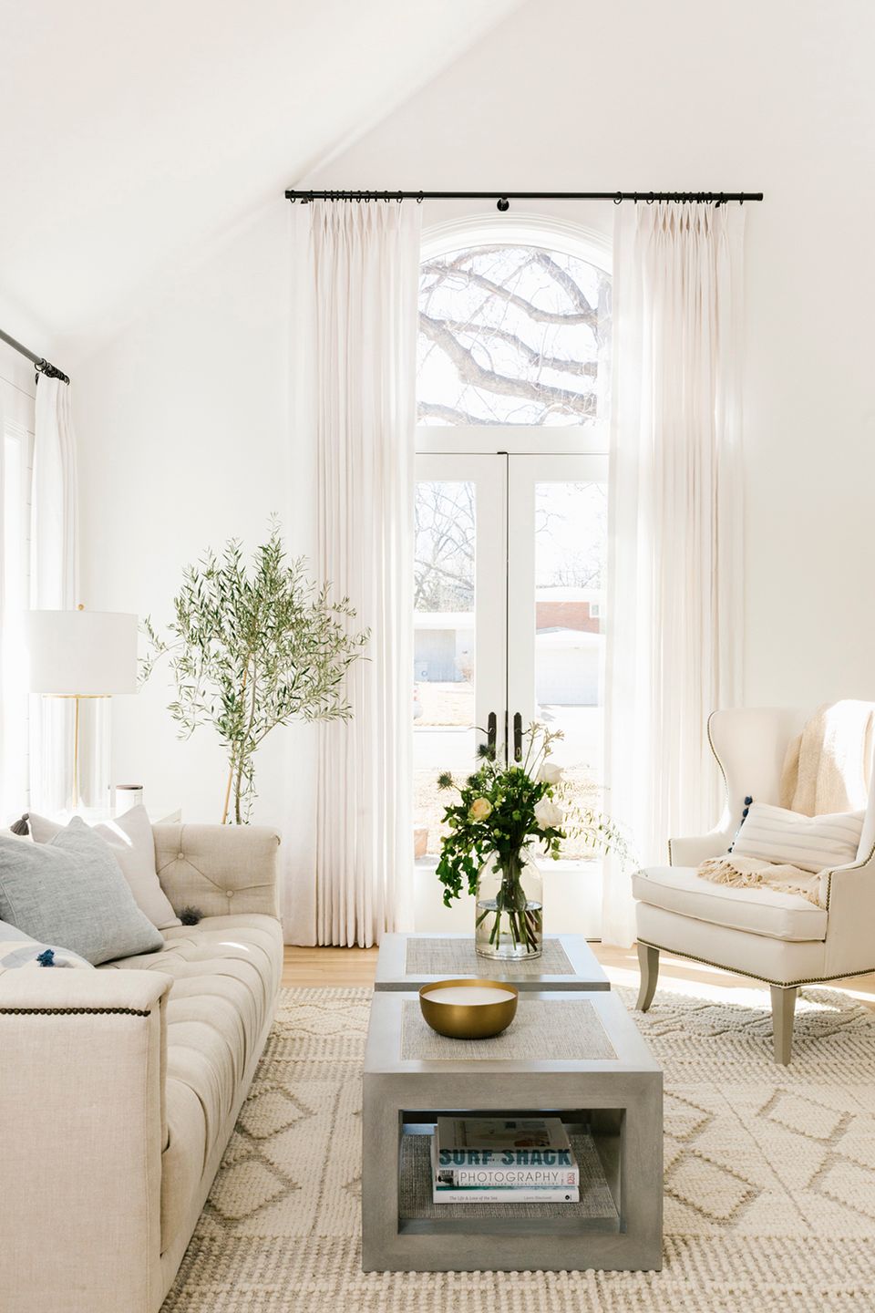 Serene minimalist living room with cream furnishings, floor-to-ceiling windows, soft florals, and neutral palette