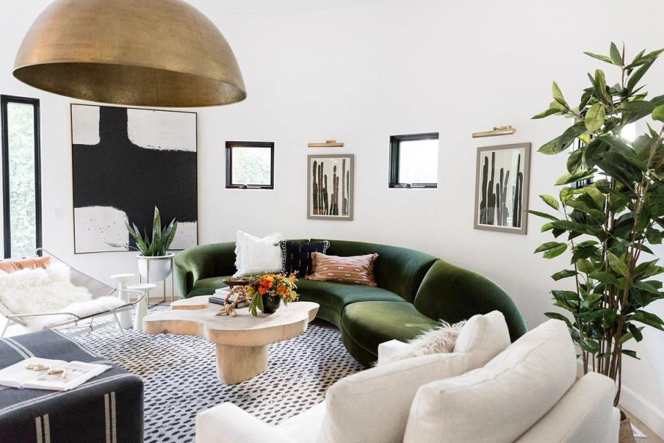 Modern living room with bold forest-green curved sofa, cream armchair, brass dome pendant, and minimalist black-framed wall art