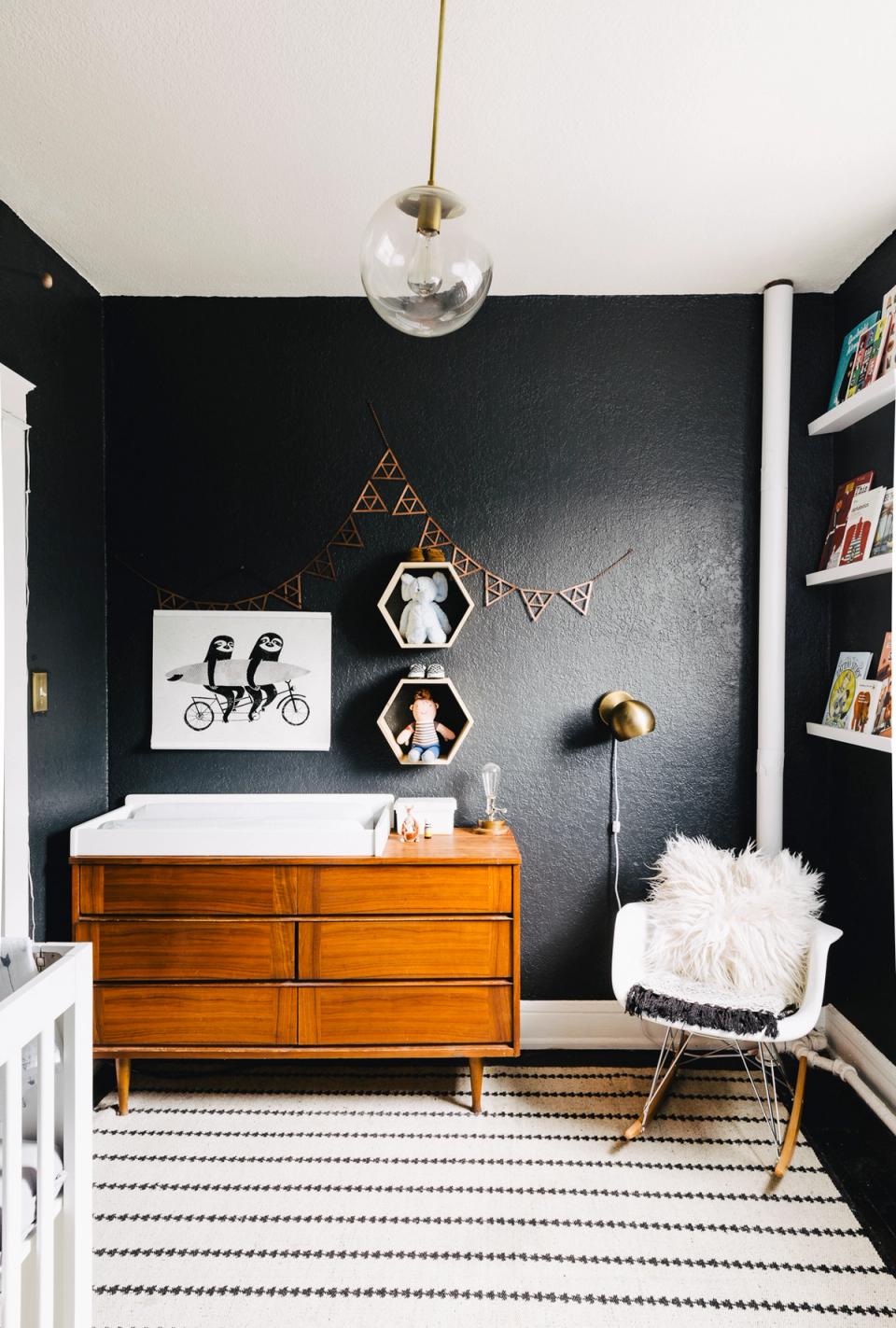 Bold modern nursery with black accent wall, mid-century wood dresser, and geometric brass wall decor