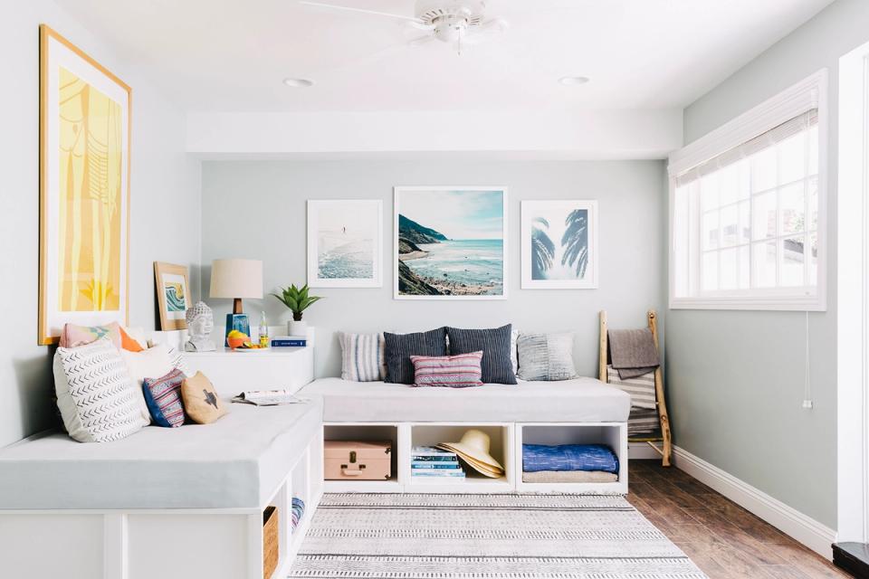 Bright coastal bedroom with gallery wall featuring landscape prints above open shelving storage unit