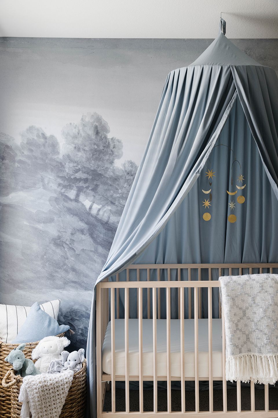 Serene nursery with gray canopy, soft mural, and woven baskets providing calm, nature-inspired toy storage solution.