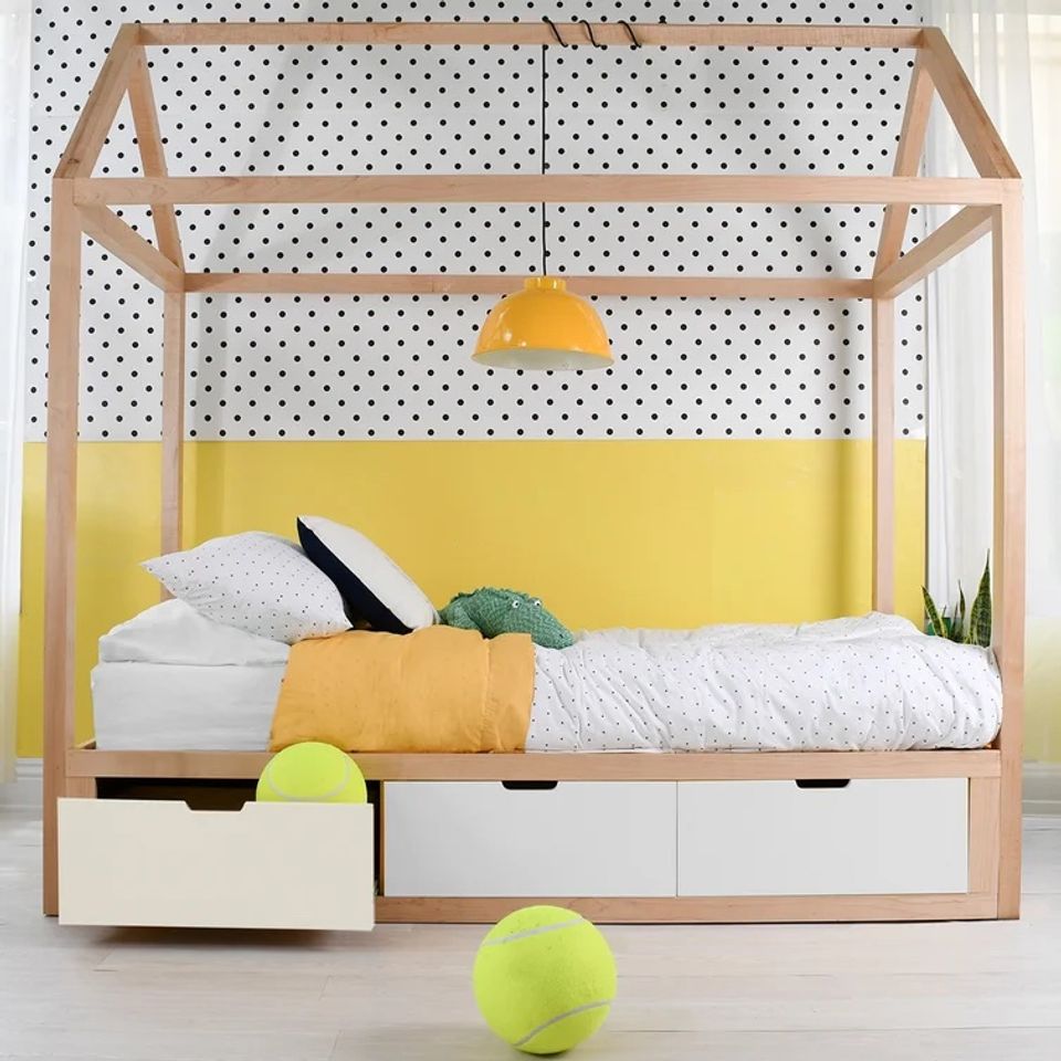 Playful kids' canopy bed in natural wood with yellow accent wall and polka dot backdrop