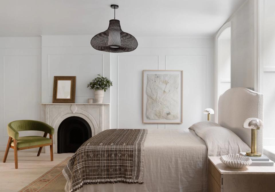 Organic modern bedroom with warm neutrals, black pendant light, olive accent chair, and natural textures creating a serene, nature-inspired retreat.