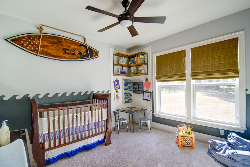 Coastal-themed nursery with surfboard decor, sage green accent wall, wooden crib, and natural light