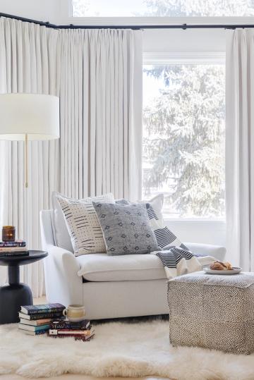 Contemporary window nook with cream upholstered chair, sheer curtains, and striped patterns in soothing neutral tones.