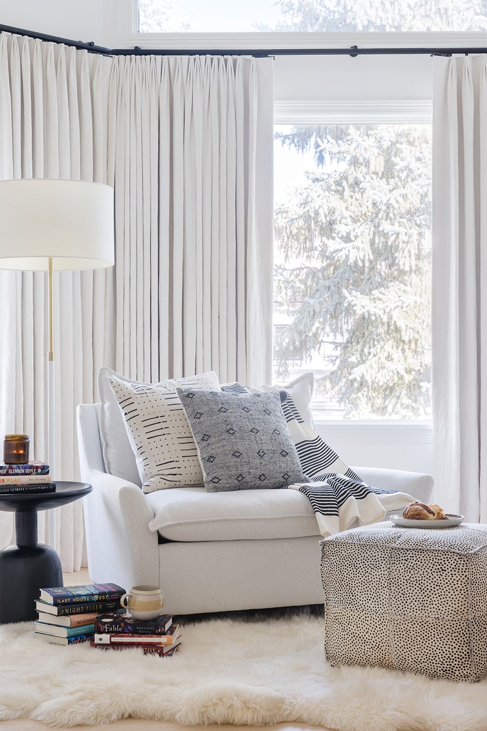 Cozy window seat with cream armchair, layered neutral and blue patterned pillows, and floor-to-ceiling sheer curtains in calming contemporary style
