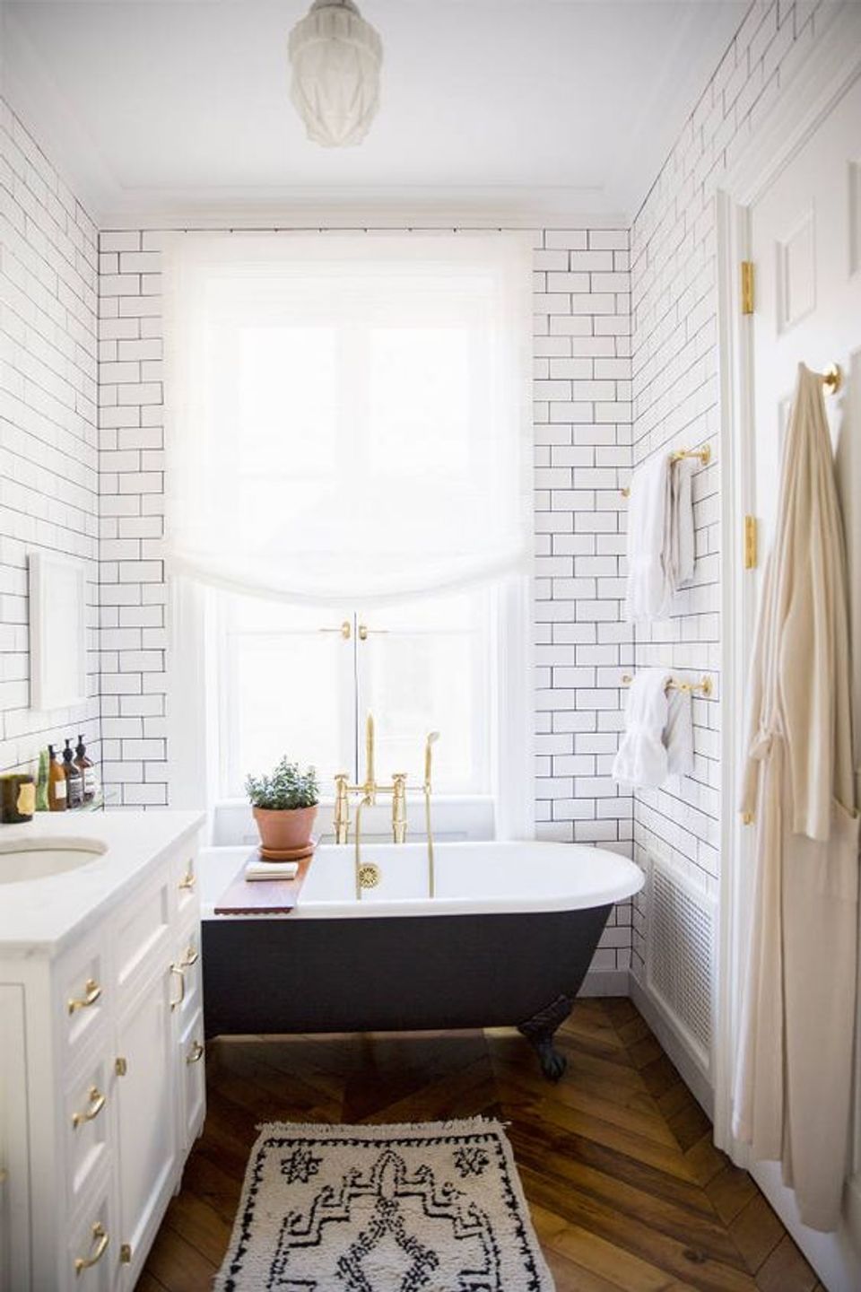 Contemporary spa-inspired bathroom with white subway tile, black soaking tub, brass hardware, and minimalist aesthetic