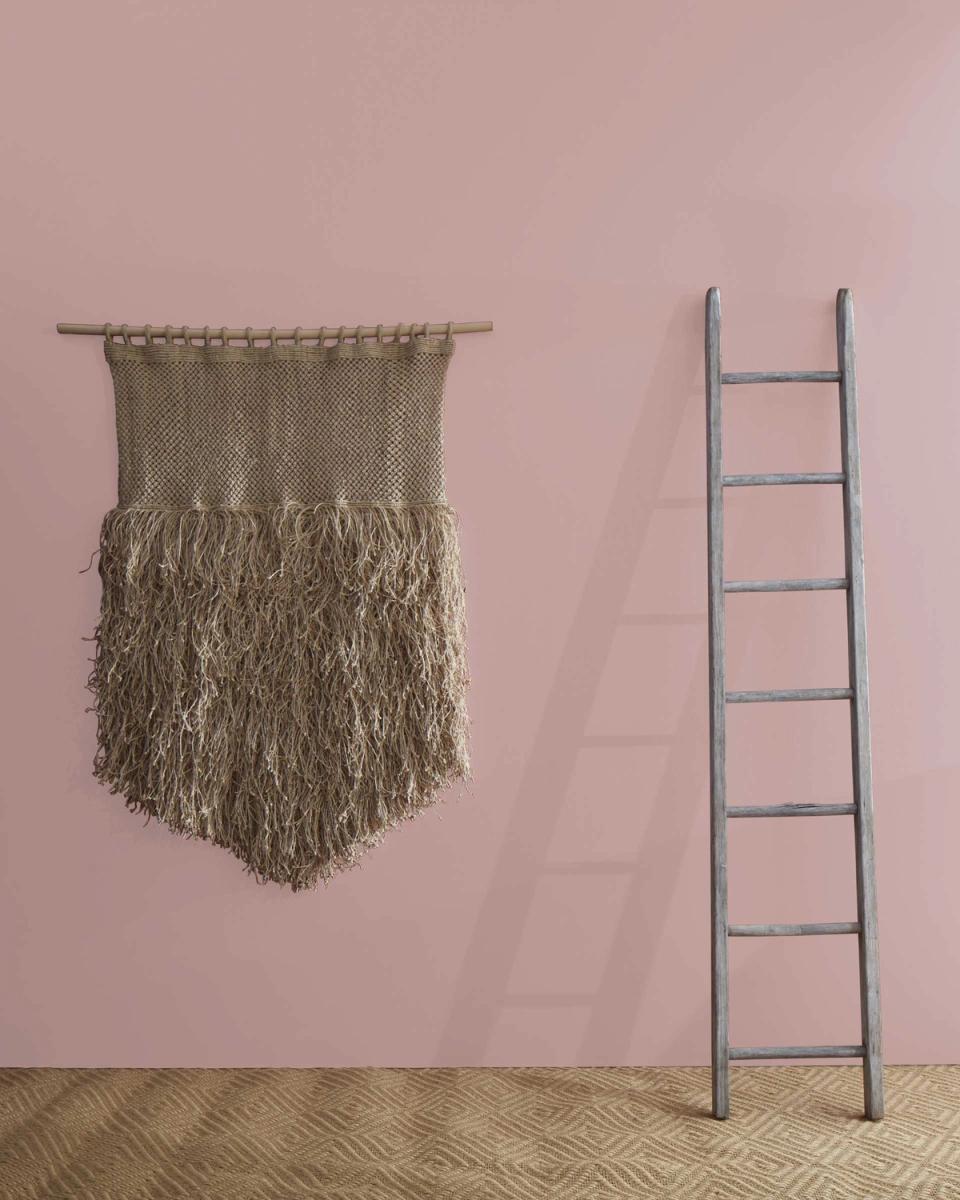 Soft mauve accent wall with woven macramé wall hanging and minimalist metal ladder creating textural contrast
