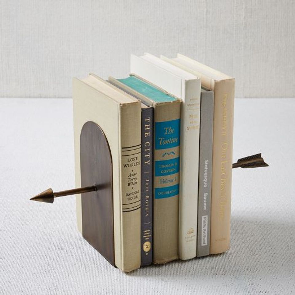 Brass arrow bookends holding vintage book collection in neutral cream and turquoise tones