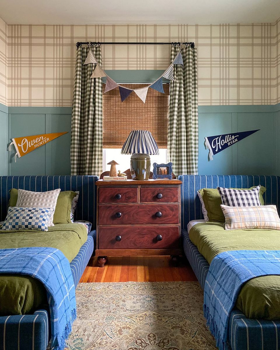 Preppy twin bedroom with plaid wallpaper, sage and blue tones, vintage pennant flags, and cherry wood dresser mixing classic Americana style