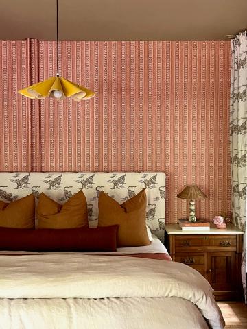 Maximalist bedroom with coral brick-pattern accent wall, golden pendant, and jewel-tone pillows