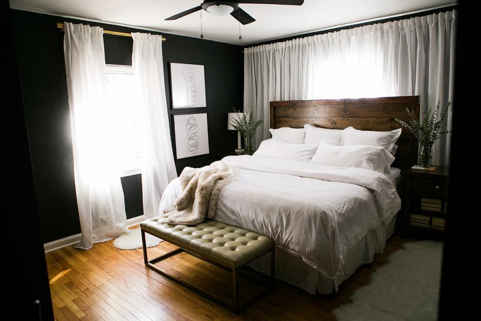 Contemporary bedroom blending dark walls with light linens, industrial bench, and soft natural lighting
