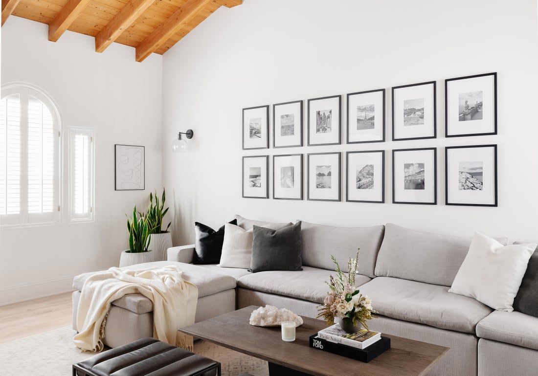 Minimalist living room with light gray sectional, exposed wood beams, white walls, and gallery wall of framed sketches