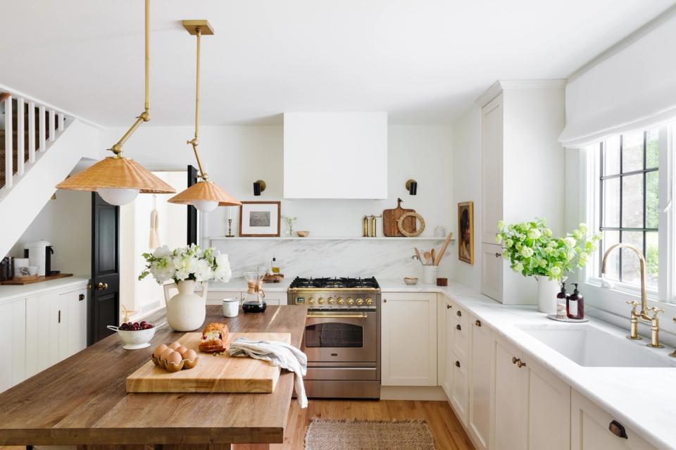 Bright farmhouse kitchen with white cabinetry, wood countertops, brass pendant lights, and natural light from large windows