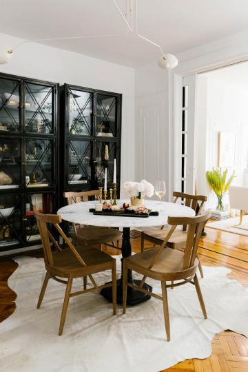 Modern dining space with crisp white palette, black glass cabinet, mid-century wood chairs, and natural light emphasis.
