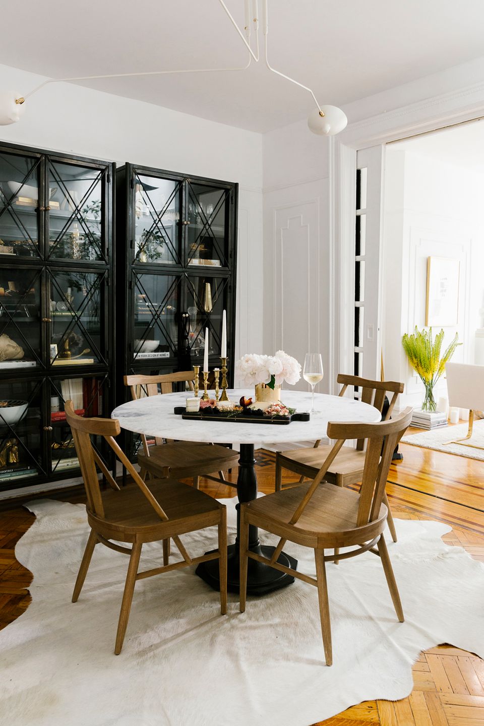 Modern dining space with crisp white palette, black glass cabinet, mid-century wood chairs, and natural light emphasis.