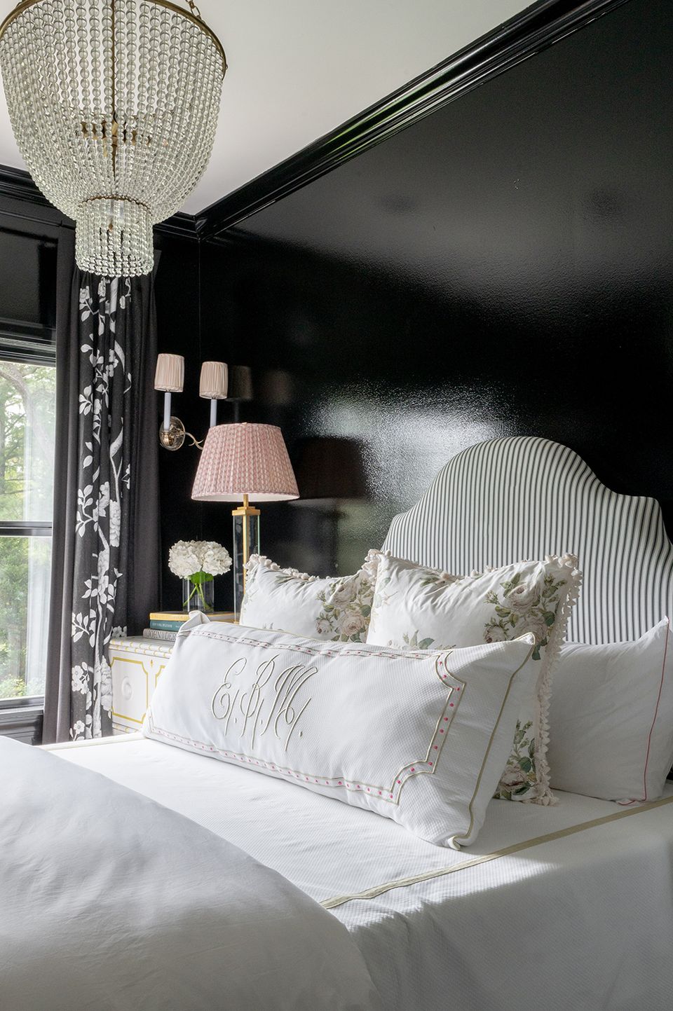 Sophisticated dark preppy bedroom with black walls, white striped headboard, crystal chandelier, and soft lighting