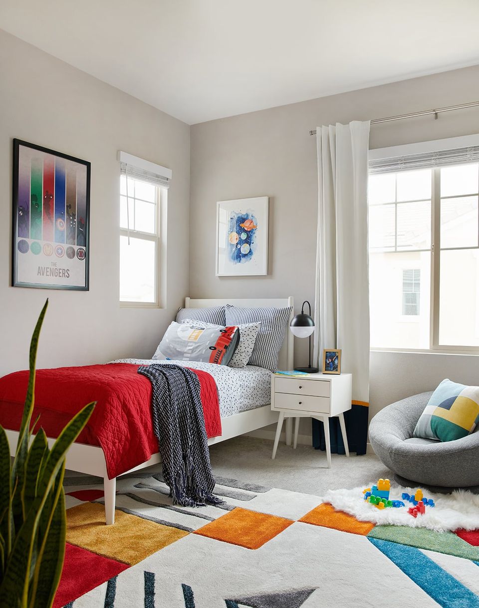 Modern kids' room with bold red bedding, colorful geometric floor rug, neutral walls, and playful pops of primary colors