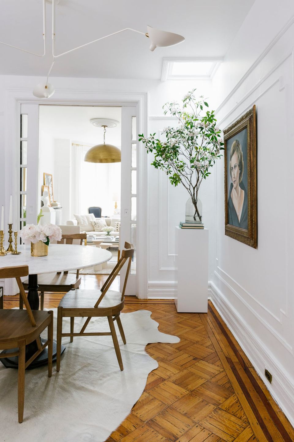 Transitional dining area with brass fixtures, natural wood flooring, herringbone patterns, and botanical elements against white wainscoting and soft neutral tones
