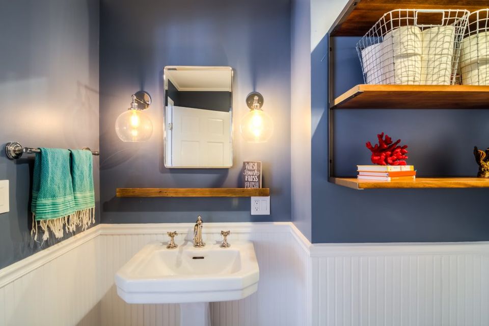 Contemporary bathroom with deep blue walls, pendant lighting, and warm wood shelving for a sophisticated spa-like atmosphere.