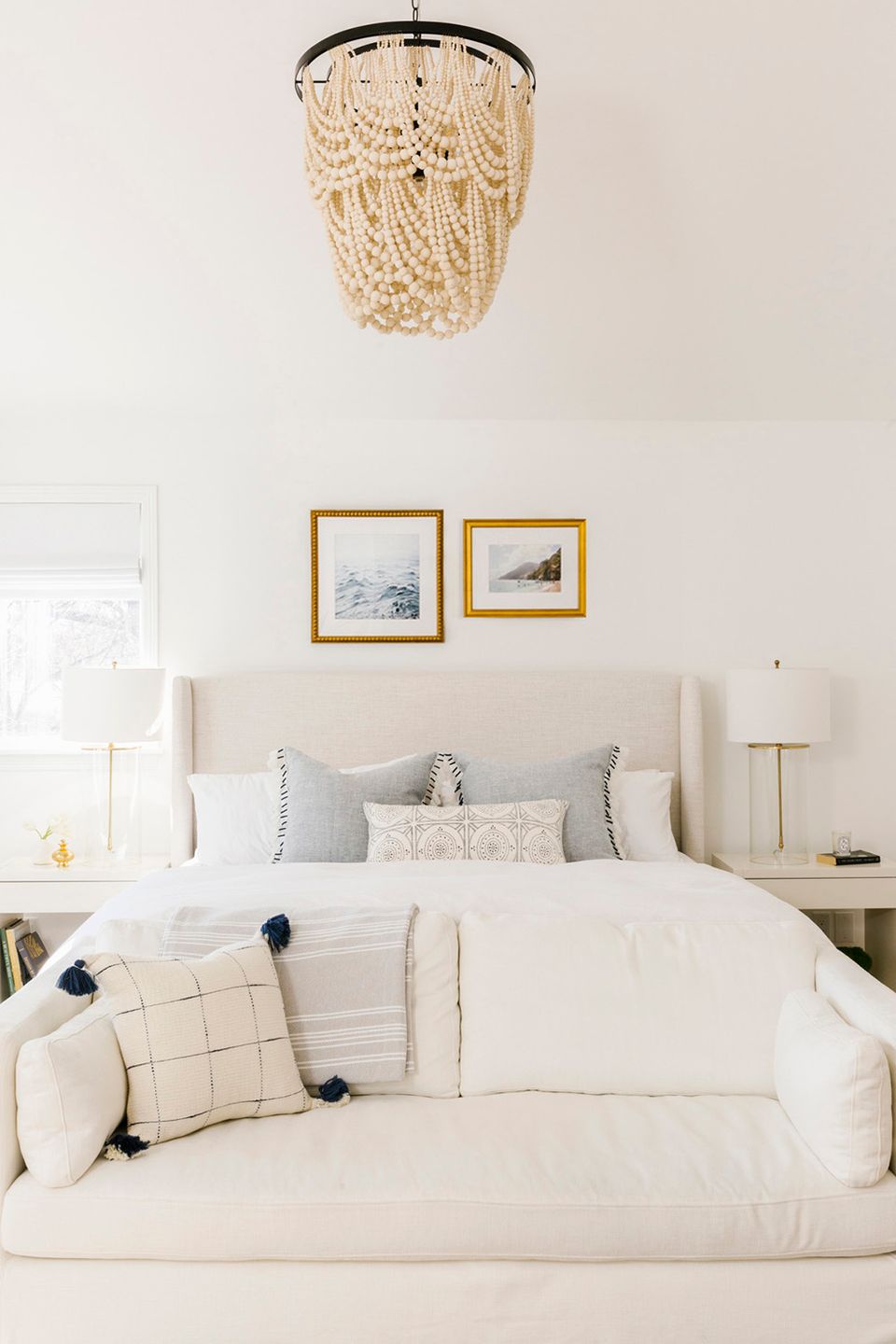 Coastal-modern bedroom with beaded macramé pendant light, gold-framed artwork, and cream tones creating a serene, textured atmosphere.