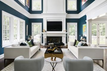 Symmetrical modern living room with deep teal walls, white fireplace surround, and balanced cream seating in a bright, airy space