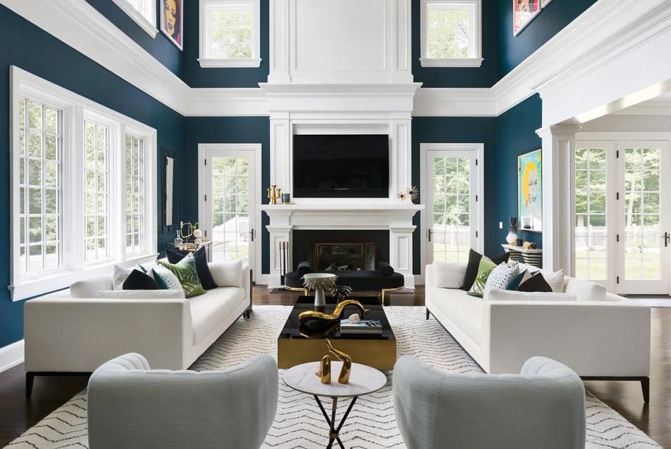 Symmetrical modern living room with deep teal walls, white fireplace surround, and balanced cream seating in a bright, airy space
