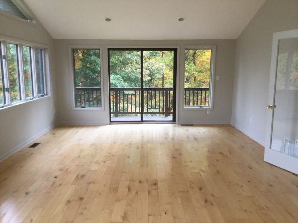 Empty dining space with light wood floors and multiple glass doors overlooking natural landscape