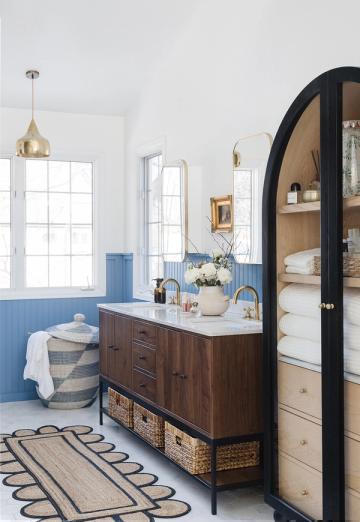 Cottage bathroom blending coastal blue accents with dark wood vanity, brass fixtures, and classic black arch mirror detail.