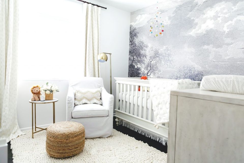 Sophisticated nursery mixing moody wallpaper, white furnishings, natural fiber basket, and brass accents.