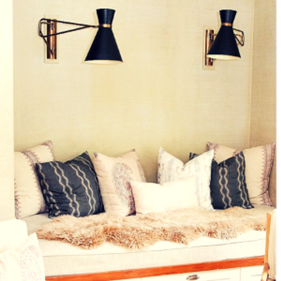 Mid-century modern daybed styled with layered sheepskin throw, geometric pillows, and black sconce lighting