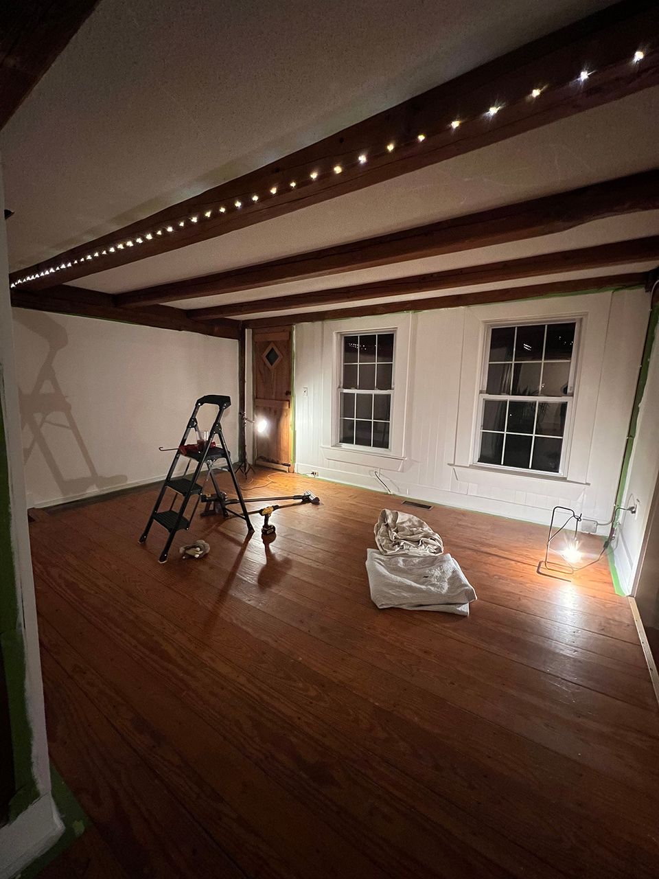 Under-construction dining space with dark wood beams, recessed lighting, and warm wood flooring