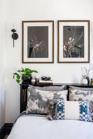 Contemporary bedroom with gallery-style framed botanical art, blue patterned pillows, and minimalist monochromatic styling