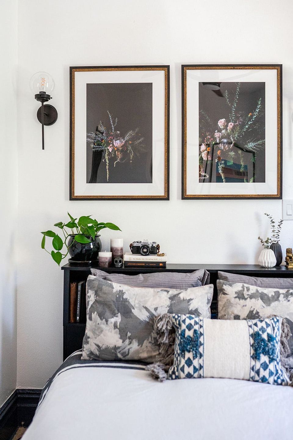 Contemporary bedroom with gallery-style framed botanical art, blue patterned pillows, and minimalist monochromatic styling