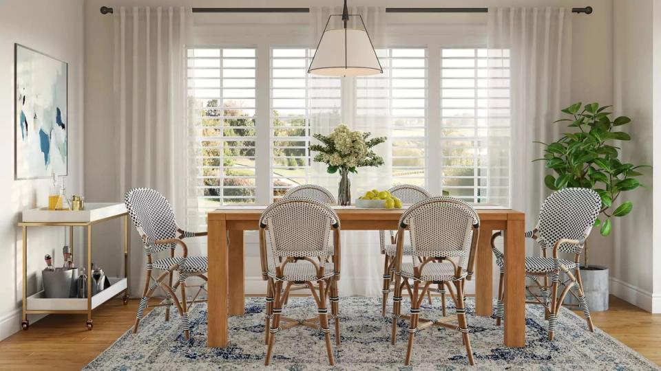 Airy coastal dining room with rattan chairs, wood table, shuttered windows, and lush plants