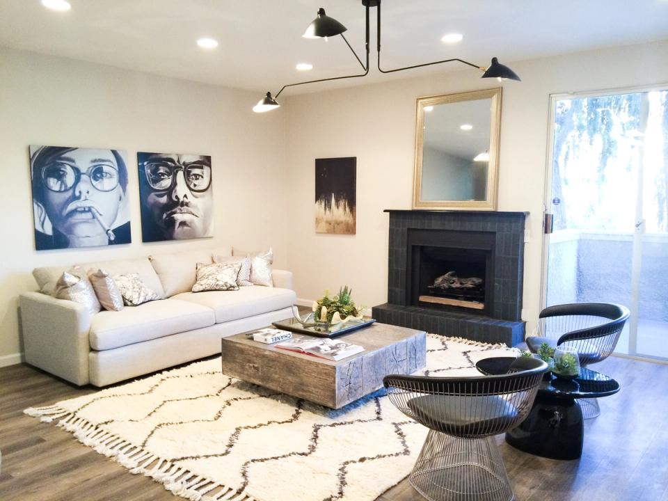 Modern living room with cream sofa, geometric rug, black fireplace, and blue-toned portrait art